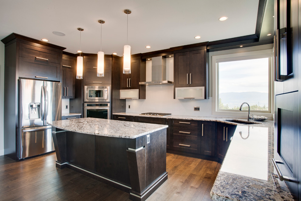 Photo of a large traditional u-shaped kitchen/diner in Vancouver with shaker cabinets, dark wood cabinets, granite worktops, white splashback, stainless steel appliances, medium hardwood flooring and an island.