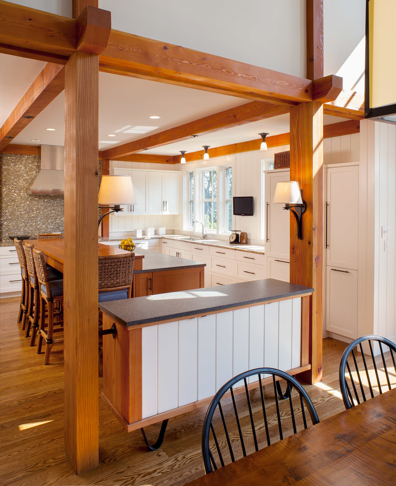 Idée de décoration pour une cuisine américaine encastrable champêtre en L de taille moyenne avec un placard avec porte à panneau encastré, des portes de placard blanches, un plan de travail en stéatite, un sol en bois brun et îlot.