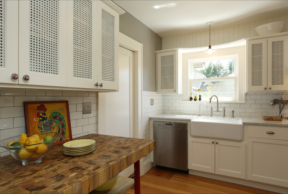 Bild på ett avskilt lantligt l-kök, med en rustik diskho, skåp i shakerstil, vita skåp, marmorbänkskiva, vitt stänkskydd, stänkskydd i tunnelbanekakel och rostfria vitvaror