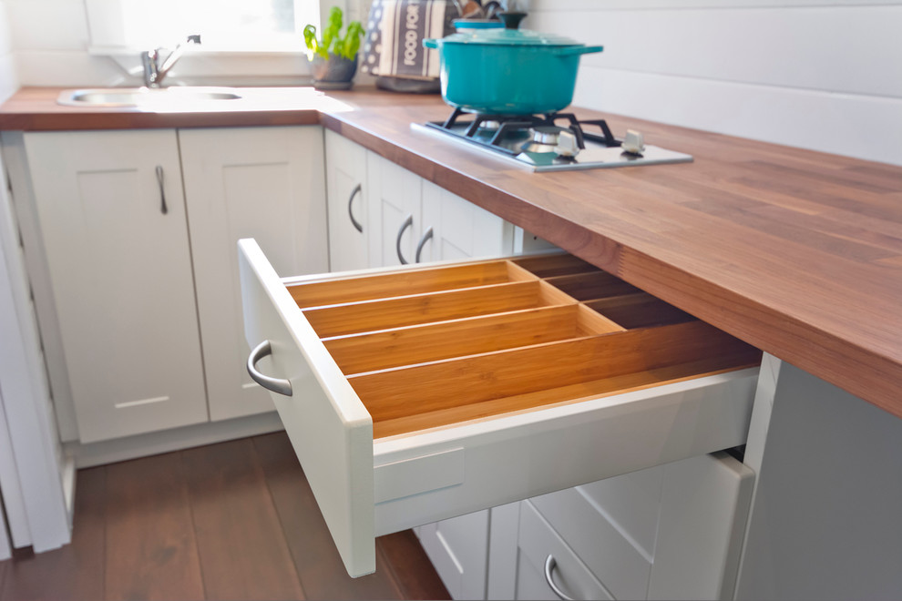 Inspiration for a small nautical l-shaped kitchen in Vancouver with a built-in sink, flat-panel cabinets, white cabinets, wood worktops, stainless steel appliances, dark hardwood flooring and no island.