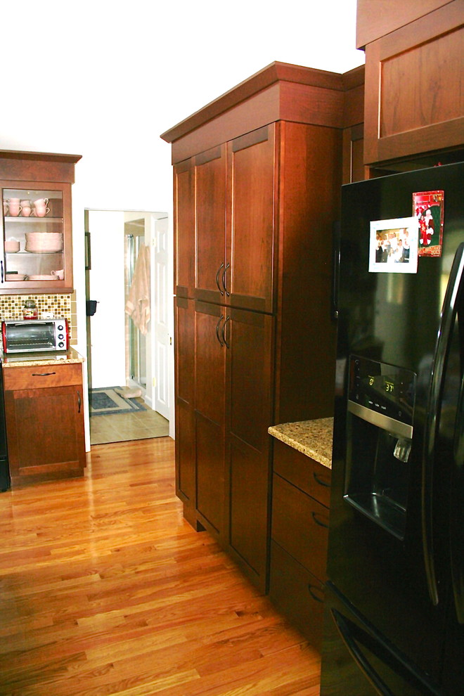 Foto på ett stort vintage kök, med en undermonterad diskho, luckor med infälld panel, skåp i mörkt trä, granitbänkskiva, flerfärgad stänkskydd, svarta vitvaror, mellanmörkt trägolv och en köksö