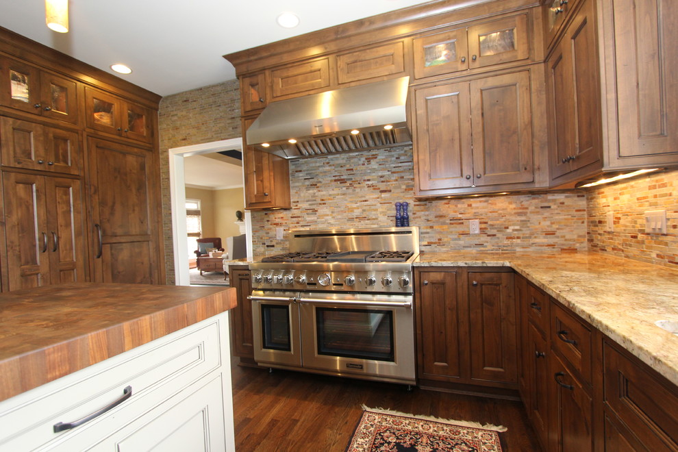 Klassisk inredning av ett stort kök och matrum, med en undermonterad diskho, skåp i mörkt trä, granitbänkskiva, brunt stänkskydd, stänkskydd i stenkakel, rostfria vitvaror, mörkt trägolv och en köksö