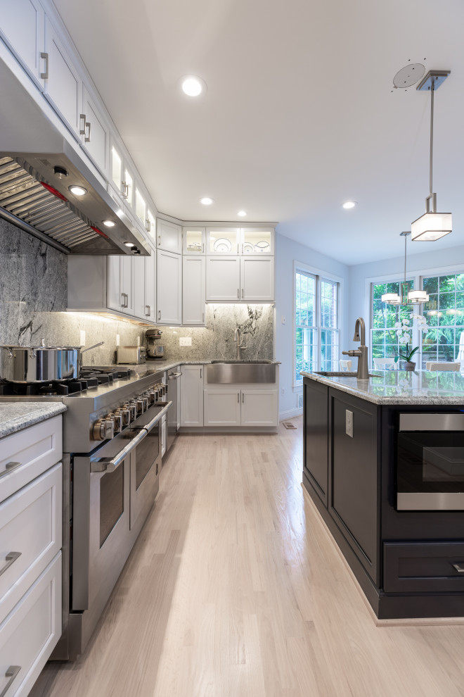 Cette image montre une cuisine américaine design de taille moyenne avec des portes de placard blanches, un plan de travail en granite, un électroménager en acier inoxydable, îlot et un sol gris.
