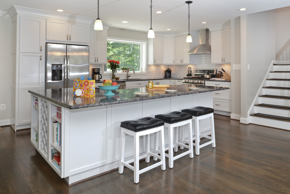 Photo of a medium sized modern l-shaped kitchen/diner in DC Metro with flat-panel cabinets, white cabinets, zinc worktops, white splashback, stainless steel appliances, an island, brown floors and black worktops.