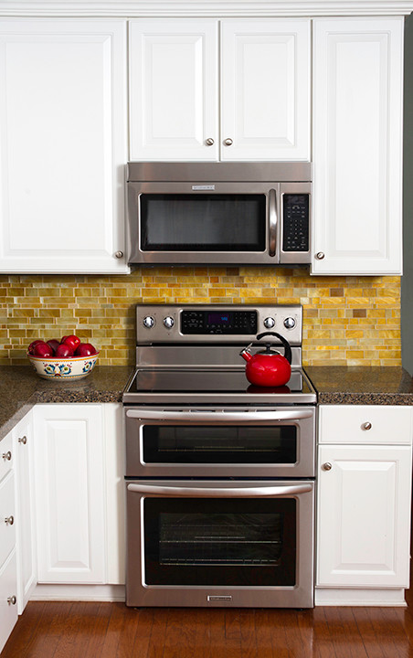Bild på ett mellanstort vintage flerfärgad flerfärgat kök, med en nedsänkt diskho, luckor med upphöjd panel, vita skåp, granitbänkskiva, brunt stänkskydd, stänkskydd i stickkakel, rostfria vitvaror, mellanmörkt trägolv, en halv köksö och brunt golv