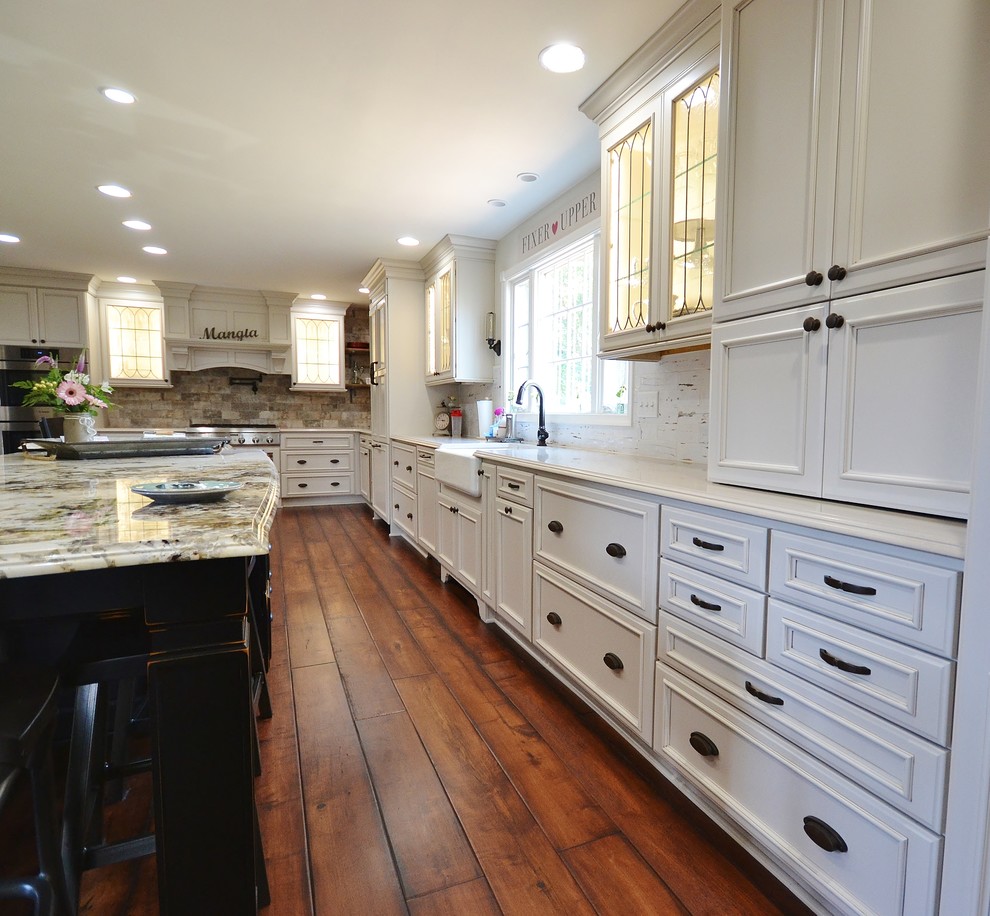 Eat-in kitchen - huge traditional l-shaped dark wood floor and brown floor eat-in kitchen idea in Philadelphia with a farmhouse sink, recessed-panel cabinets, white cabinets, granite countertops, beige backsplash, stone tile backsplash, stainless steel appliances, two islands and multicolored countertops