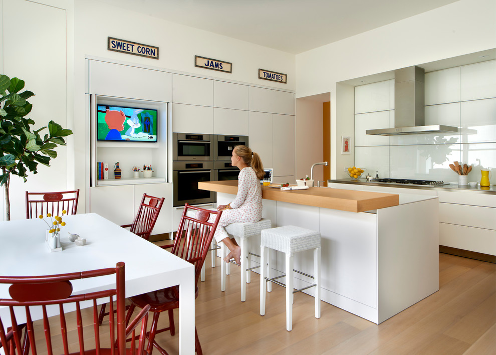 Example of a trendy light wood floor eat-in kitchen design in Chicago with flat-panel cabinets, white cabinets, white backsplash, glass sheet backsplash, stainless steel appliances and an island