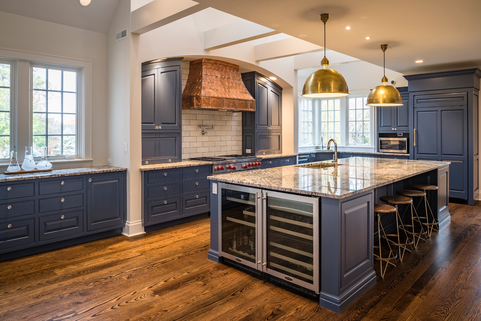Exempel på ett mellanstort modernt grå grått kök, med en dubbel diskho, luckor med upphöjd panel, blå skåp, granitbänkskiva, vitt stänkskydd, stänkskydd i tunnelbanekakel, integrerade vitvaror, mellanmörkt trägolv, en köksö och brunt golv