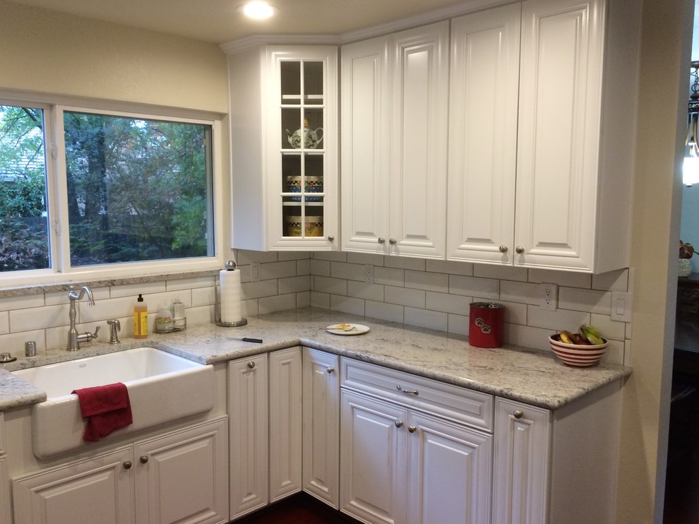 This is an example of a medium sized traditional l-shaped kitchen/diner in Sacramento with a belfast sink, raised-panel cabinets, white cabinets, engineered stone countertops, multi-coloured splashback, stainless steel appliances, medium hardwood flooring and no island.