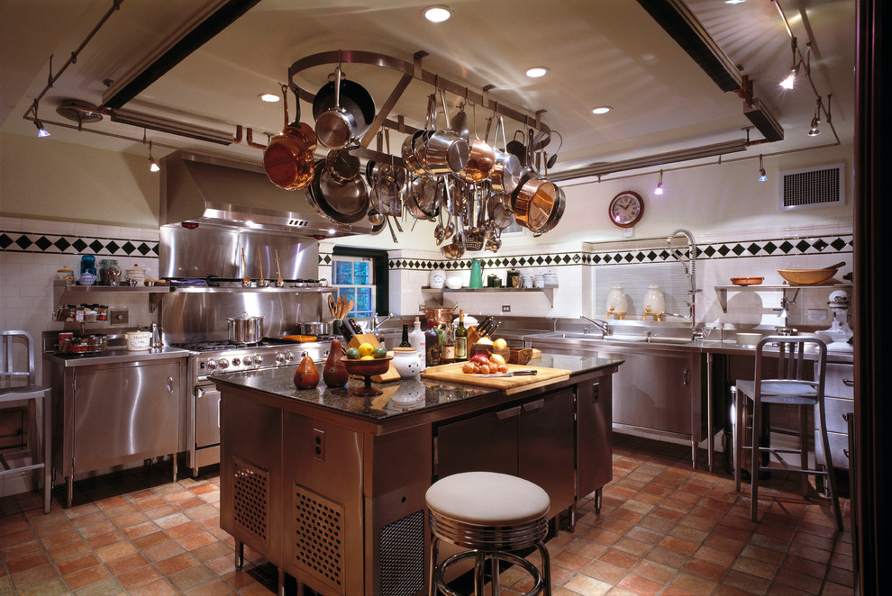 Klassisk inredning av ett avskilt u-kök, med en nedsänkt diskho, luckor med profilerade fronter, skåp i rostfritt stål, granitbänkskiva, vitt stänkskydd, stänkskydd i keramik, rostfria vitvaror, klinkergolv i terrakotta och en köksö