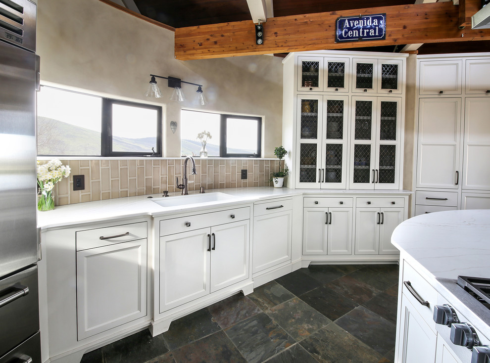Inspiration for a large country kitchen in San Francisco with a submerged sink, recessed-panel cabinets, white cabinets, engineered stone countertops, beige splashback, porcelain splashback, stainless steel appliances, slate flooring, an island, multi-coloured floors and white worktops.