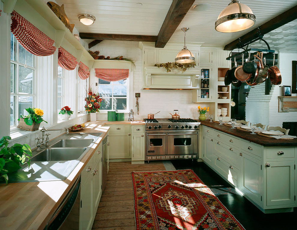 デンバーにある高級な広いカントリー風のおしゃれなキッチン (ドロップインシンク、落し込みパネル扉のキャビネット、青いキャビネット、木材カウンター、白いキッチンパネル、レンガのキッチンパネル、シルバーの調理設備、無垢フローリング、茶色い床、茶色いキッチンカウンター) の写真