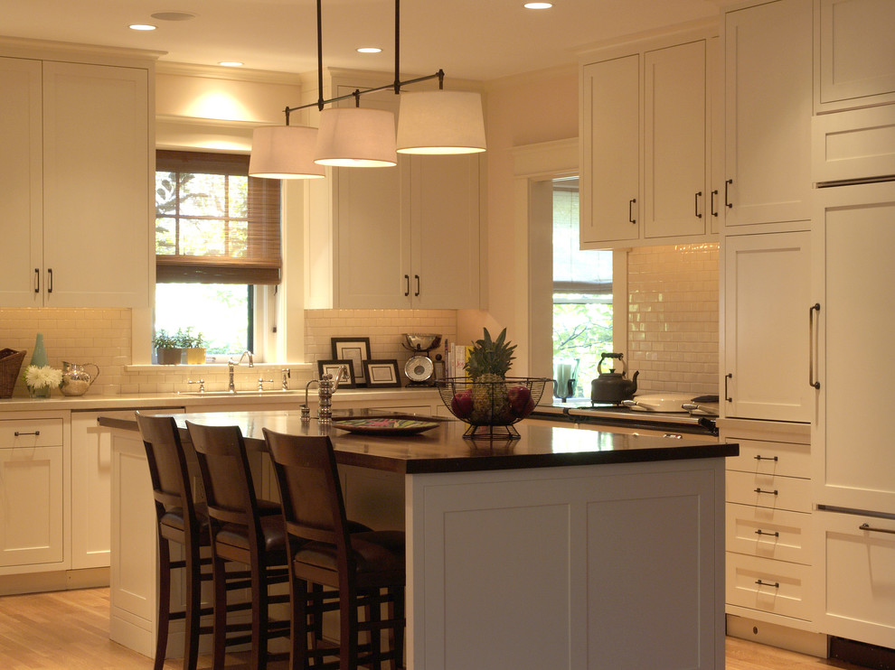 Photo of a traditional u-shaped enclosed kitchen in Denver with shaker cabinets, white cabinets, integrated appliances, light hardwood flooring and an island.