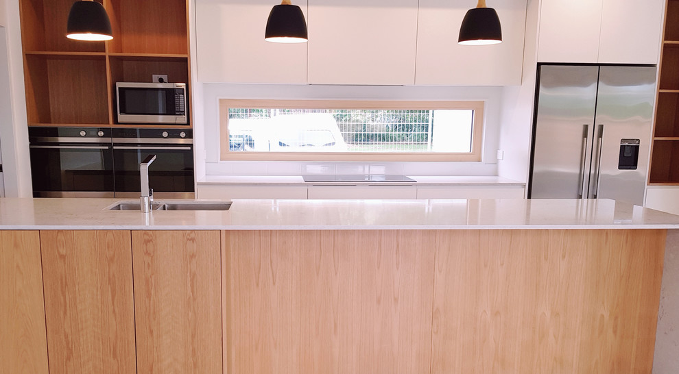 Exempel på ett stort modernt kök, med en undermonterad diskho, släta luckor, vita skåp, bänkskiva i kvartsit, vitt stänkskydd, stänkskydd i sten, rostfria vitvaror, ljust trägolv, en köksö och brunt golv
