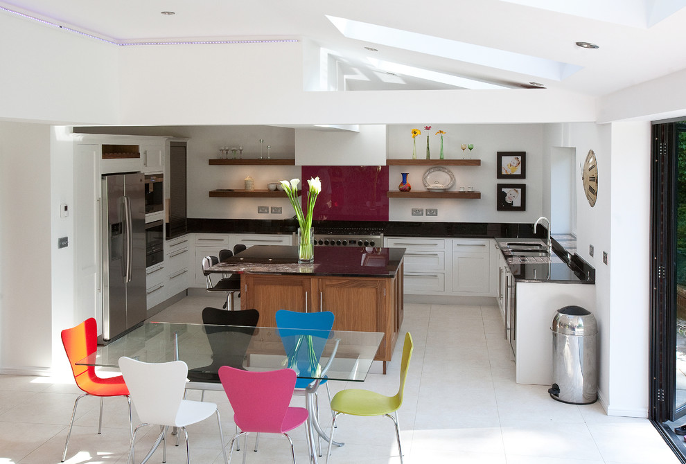 Foto på ett stort funkis kök, med en dubbel diskho, luckor med infälld panel, vita skåp, granitbänkskiva, rött stänkskydd, glaspanel som stänkskydd, rostfria vitvaror, klinkergolv i keramik och en köksö