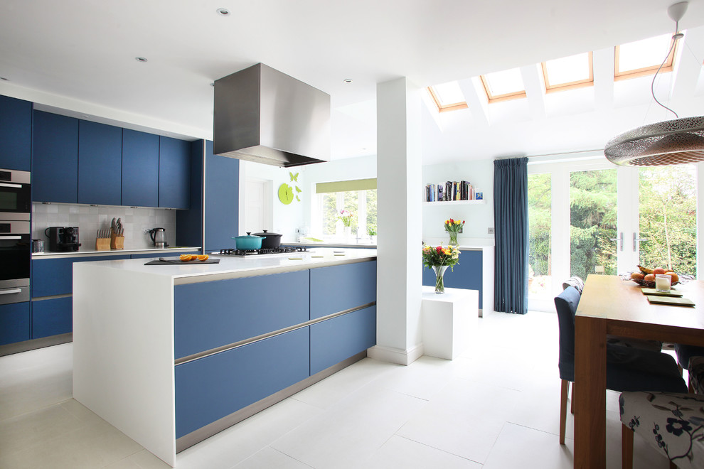 Ejemplo de cocina comedor moderna con armarios con paneles lisos, puertas de armario azules, salpicadero verde y electrodomésticos de acero inoxidable