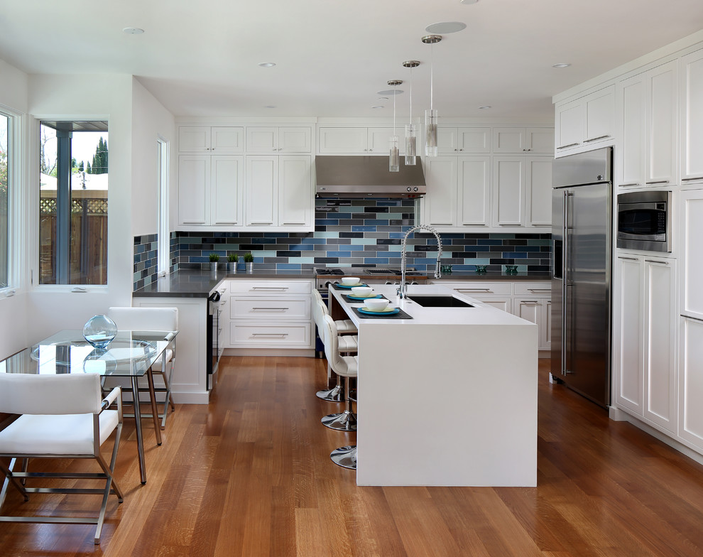 Bild på ett mellanstort funkis kök, med en undermonterad diskho, skåp i shakerstil, vita skåp, bänkskiva i kvarts, rostfria vitvaror, mellanmörkt trägolv, en köksö och flerfärgad stänkskydd