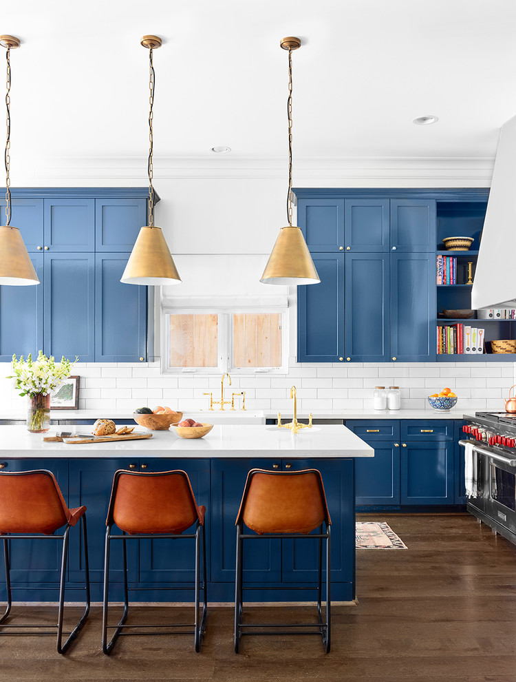 Klassische Küche in L-Form mit Schrankfronten im Shaker-Stil, blauen Schränken, Küchenrückwand in Weiß, Rückwand aus Metrofliesen, Küchengeräten aus Edelstahl, dunklem Holzboden, Kücheninsel und braunem Boden