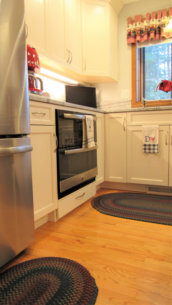 Klassisk inredning av ett mellanstort grå grått kök, med en undermonterad diskho, luckor med infälld panel, vita skåp, granitbänkskiva, grått stänkskydd, rostfria vitvaror, ljust trägolv, en köksö och brunt golv