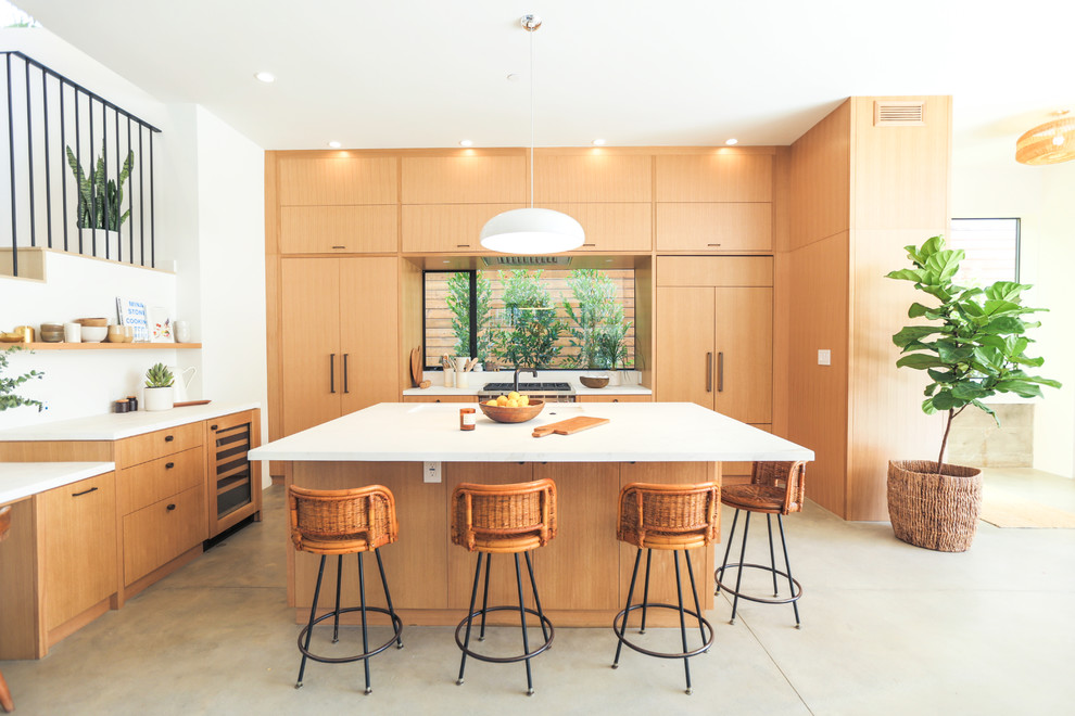 Idéer för ett modernt kök, med en undermonterad diskho, släta luckor, skåp i ljust trä, fönster som stänkskydd, integrerade vitvaror, betonggolv, en köksö och grått golv