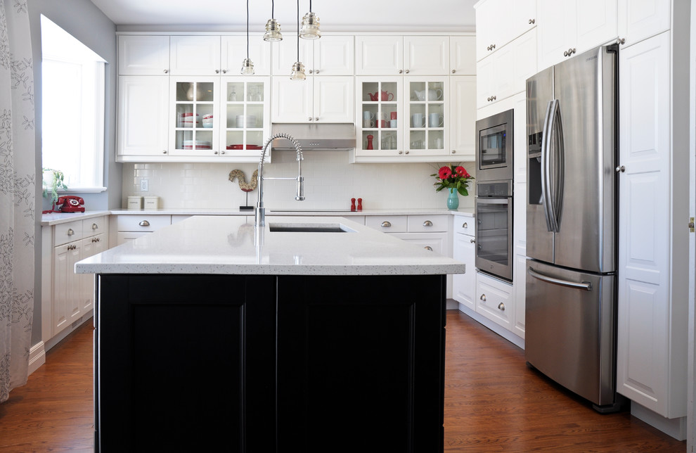Bild på ett vintage kök och matrum, med en undermonterad diskho, luckor med upphöjd panel, vita skåp, bänkskiva i kvarts, vitt stänkskydd, stänkskydd i porslinskakel, rostfria vitvaror och en köksö