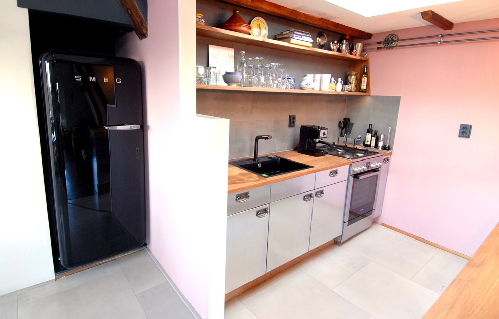 Idee per una cucina industriale di medie dimensioni con lavello integrato, ante in acciaio inossidabile, top in legno, paraspruzzi grigio, pavimento in laminato e pavimento beige