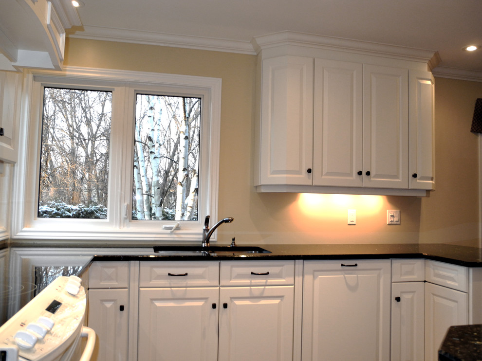 Idéer för att renovera ett avskilt, mellanstort funkis l-kök, med en undermonterad diskho, luckor med profilerade fronter, vita skåp, granitbänkskiva, beige stänkskydd, vita vitvaror, mörkt trägolv och en halv köksö