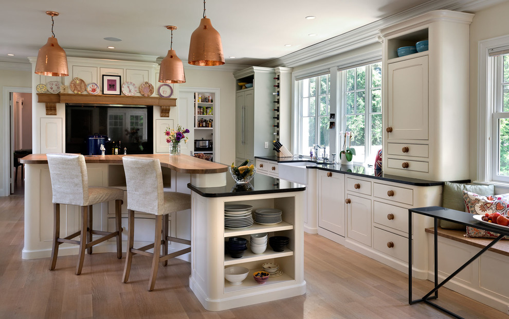 Klassische Wohnküche in L-Form mit Landhausspüle, Kassettenfronten, weißen Schränken, braunem Holzboden und Kücheninsel in Boston