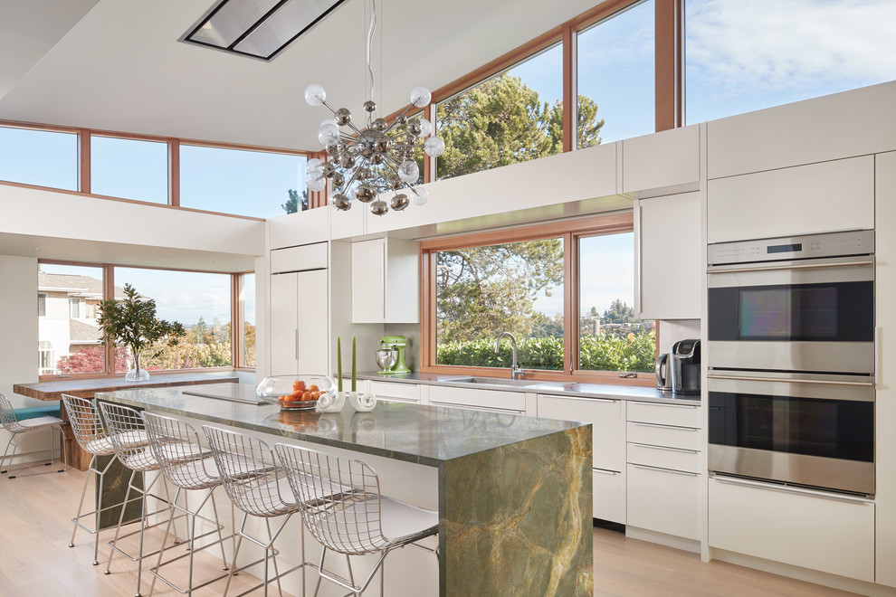 Moderne Küche in L-Form mit flächenbündigen Schrankfronten, weißen Schränken, Rückwand-Fenster, Küchengeräten aus Edelstahl, braunem Holzboden, Kücheninsel und braunem Boden in Sonstige