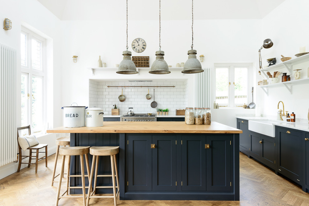 Foto på ett vintage kök, med en rustik diskho, skåp i shakerstil, blå skåp, träbänkskiva, vitt stänkskydd, stänkskydd i tunnelbanekakel, rostfria vitvaror, mellanmörkt trägolv och en köksö