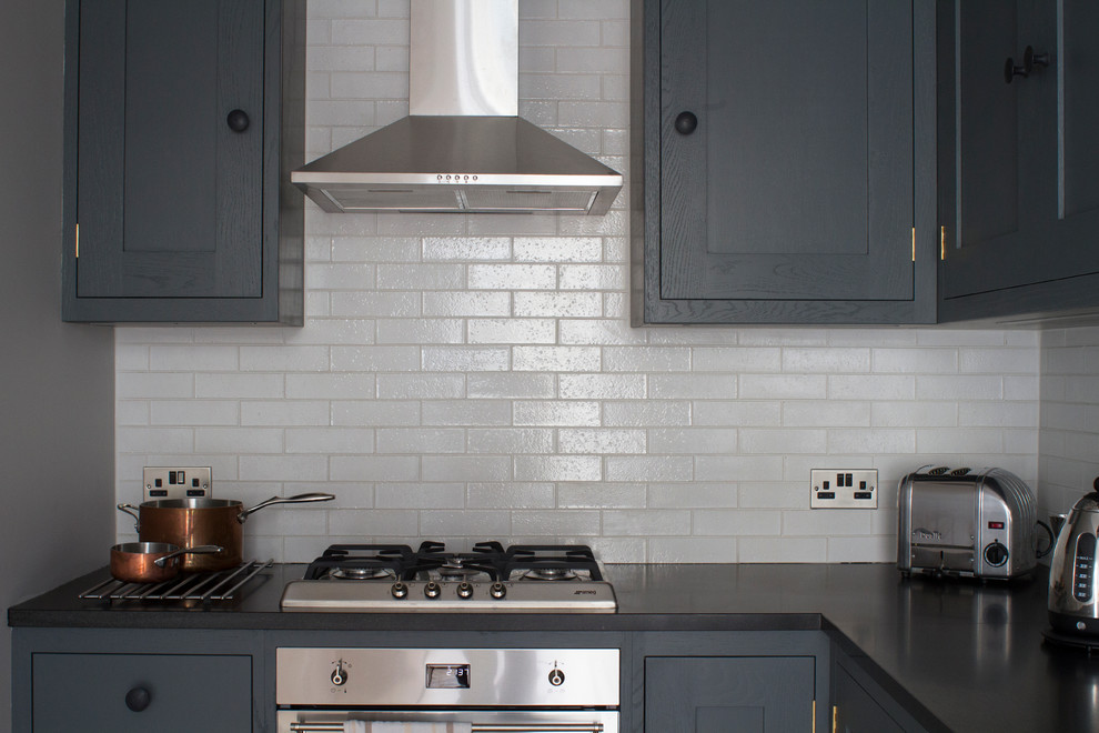 Bild på ett avskilt, litet funkis l-kök, med en undermonterad diskho, skåp i shakerstil, granitbänkskiva, vitt stänkskydd, rostfria vitvaror, mellanmörkt trägolv, grå skåp och stänkskydd i tunnelbanekakel
