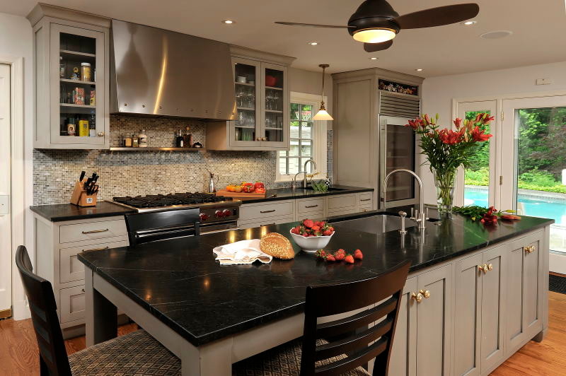 Klassisk inredning av ett kök, med en undermonterad diskho, luckor med infälld panel, grå skåp, grått stänkskydd, rostfria vitvaror och en köksö