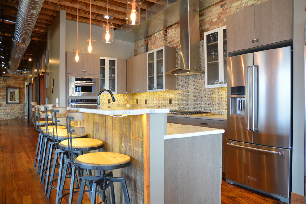 Example of a large urban l-shaped medium tone wood floor and brown floor eat-in kitchen design in Other with a farmhouse sink, flat-panel cabinets, gray cabinets, quartz countertops, multicolored backsplash, mosaic tile backsplash, stainless steel appliances and an island