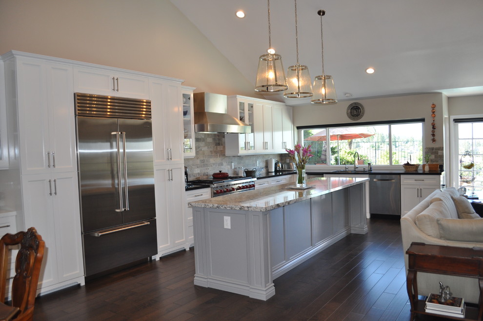 Inspiration for a mid-sized transitional l-shaped dark wood floor and brown floor open concept kitchen remodel in Orange County with a double-bowl sink, shaker cabinets, white cabinets, granite countertops, gray backsplash, stone tile backsplash, stainless steel appliances and an island