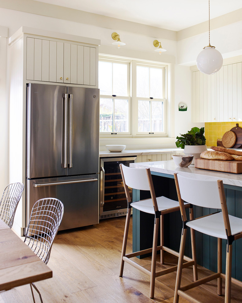 Example of a large farmhouse l-shaped medium tone wood floor eat-in kitchen design in San Francisco with a farmhouse sink, flat-panel cabinets, beige cabinets, quartzite countertops, yellow backsplash, terra-cotta backsplash, stainless steel appliances, an island and white countertops