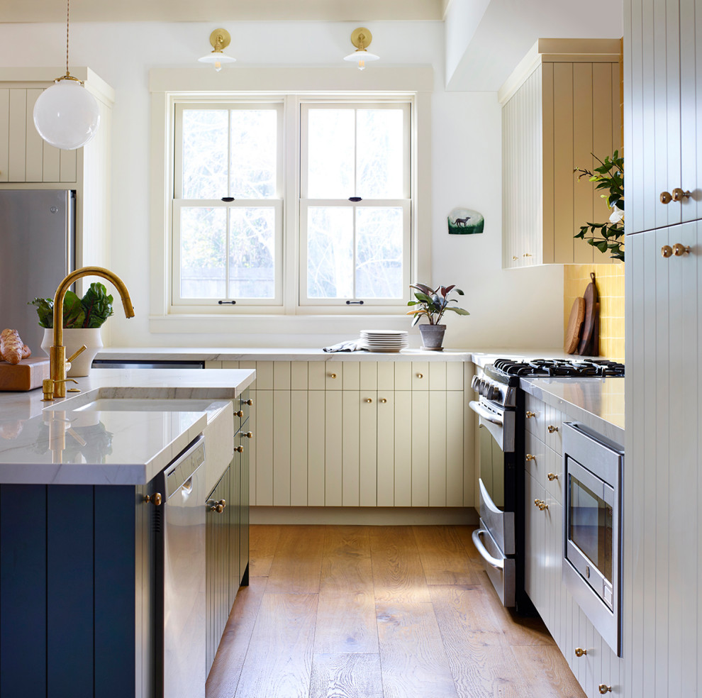 Large cottage l-shaped medium tone wood floor eat-in kitchen photo in San Francisco with a farmhouse sink, flat-panel cabinets, beige cabinets, quartzite countertops, yellow backsplash, terra-cotta backsplash, stainless steel appliances, an island and white countertops