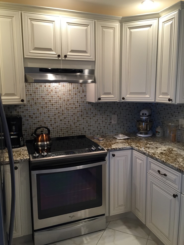 Inredning av ett klassiskt mellanstort kök, med en dubbel diskho, luckor med upphöjd panel, vita skåp, granitbänkskiva, flerfärgad stänkskydd, stänkskydd i mosaik, rostfria vitvaror, klinkergolv i porslin och en köksö