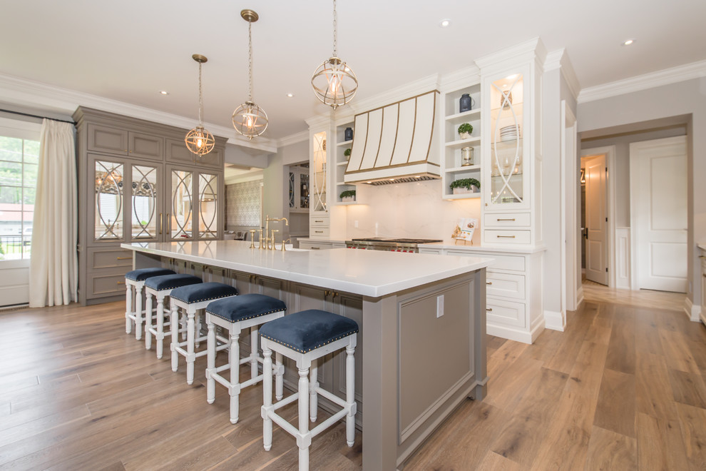 Zweizeilige Klassische Küche mit Landhausspüle, Schrankfronten im Shaker-Stil, weißen Schränken, Küchenrückwand in Weiß, Rückwand aus Stein, braunem Holzboden, Kücheninsel und braunem Boden in Toronto