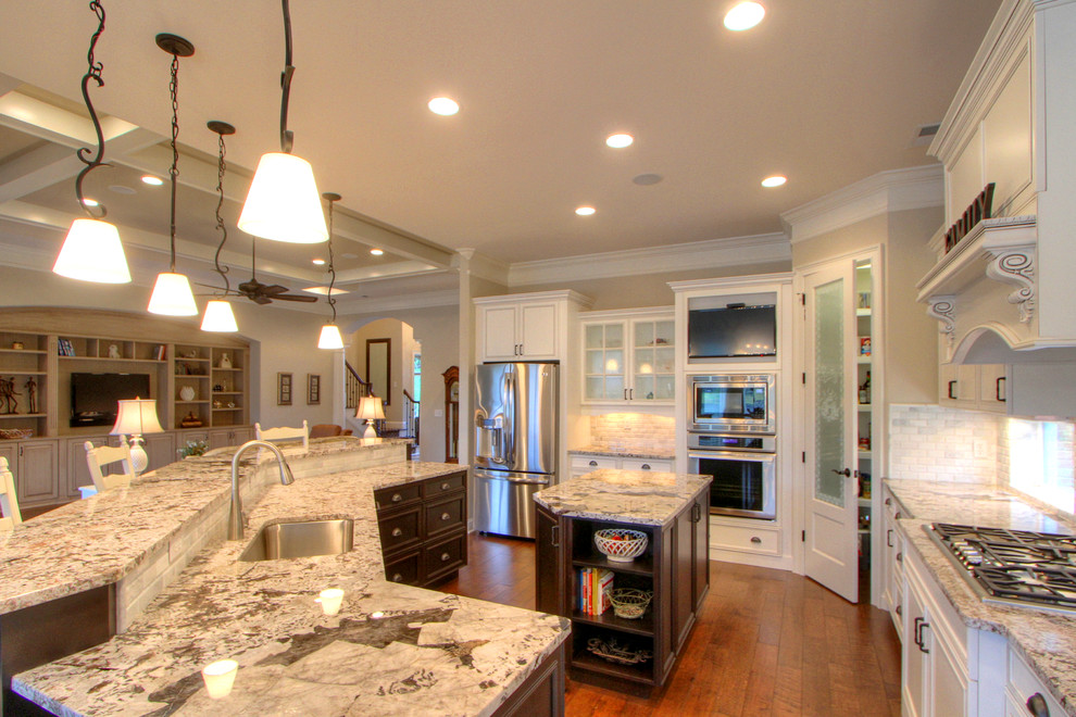 This is an example of a large classic kitchen in Atlanta with white cabinets, white splashback, stainless steel appliances, medium hardwood flooring and multiple islands.