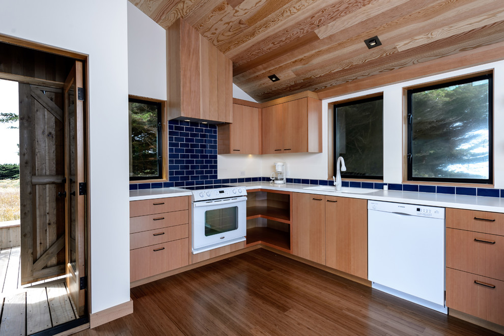 Réalisation d'une cuisine design en bois brun avec un électroménager blanc, un placard à porte plane, une crédence bleue et une crédence en carrelage métro.