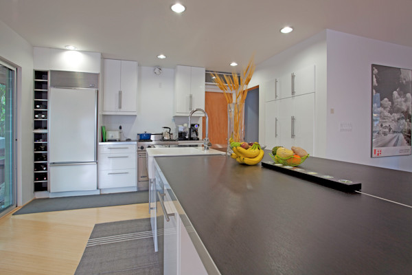 Small contemporary l-shaped open plan kitchen in Los Angeles with a belfast sink, flat-panel cabinets, white cabinets, engineered stone countertops, white splashback, porcelain splashback, stainless steel appliances, light hardwood flooring and an island.