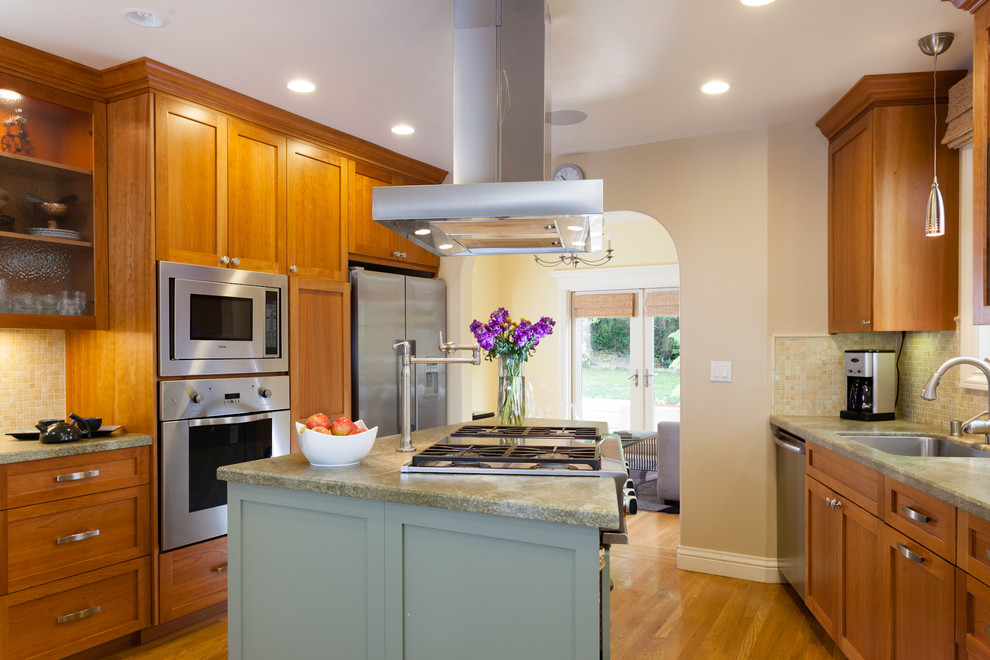 Foto på ett mellanstort eklektiskt grön kök, med en undermonterad diskho, skåp i shakerstil, skåp i ljust trä, granitbänkskiva, grönt stänkskydd, stänkskydd i glaskakel, rostfria vitvaror, ljust trägolv, en köksö och brunt golv