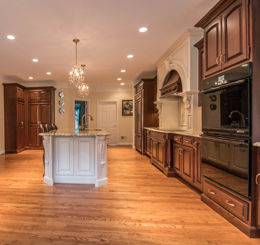 Example of a huge classic kitchen design in DC Metro with an undermount sink, raised-panel cabinets, dark wood cabinets, granite countertops, beige backsplash, ceramic backsplash, black appliances and an island