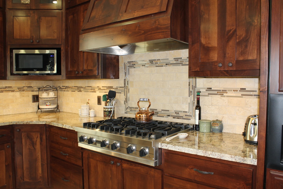 Example of a large mountain style l-shaped travertine floor eat-in kitchen design in San Luis Obispo with a farmhouse sink, recessed-panel cabinets, dark wood cabinets, granite countertops, beige backsplash, stone tile backsplash, stainless steel appliances and an island