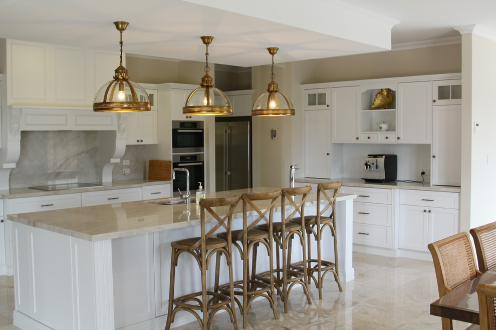 Immagine di una cucina chic con lavello sottopiano, ante in stile shaker, ante bianche, paraspruzzi beige, elettrodomestici da incasso, pavimento beige e top beige