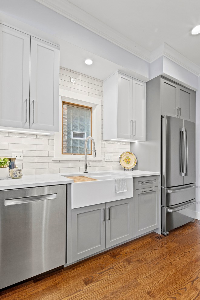 Mid-sized transitional galley medium tone wood floor and brown floor open concept kitchen photo in Chicago with a farmhouse sink, shaker cabinets, gray cabinets, quartz countertops, white backsplash, ceramic backsplash, stainless steel appliances, no island and white countertops