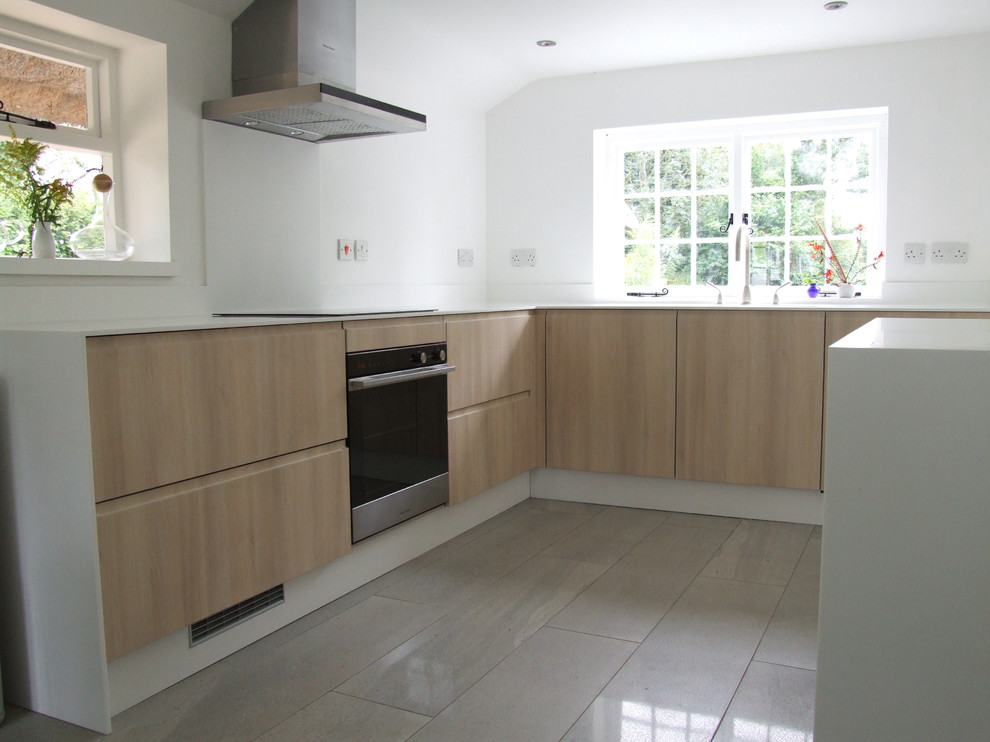 This is an example of a medium sized contemporary l-shaped kitchen/diner in Dorset with a submerged sink, flat-panel cabinets, light wood cabinets, composite countertops, white splashback, stainless steel appliances, limestone flooring and no island.
