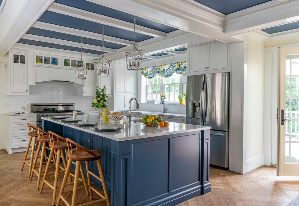 Inredning av ett klassiskt vit vitt kök, med en rustik diskho, luckor med profilerade fronter, blå skåp, vitt stänkskydd, rostfria vitvaror, mellanmörkt trägolv, en köksö och brunt golv