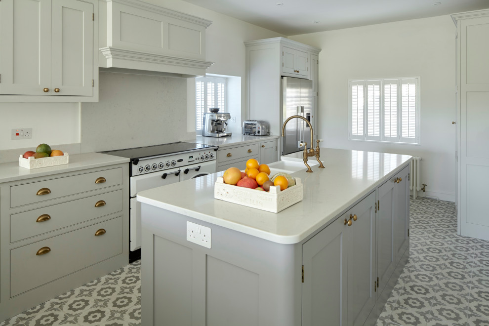 Example of a mid-sized transitional ceramic tile and multicolored floor kitchen design in Hampshire with a farmhouse sink, shaker cabinets, gray cabinets, quartzite countertops, stone slab backsplash, an island, white countertops, gray backsplash and white appliances