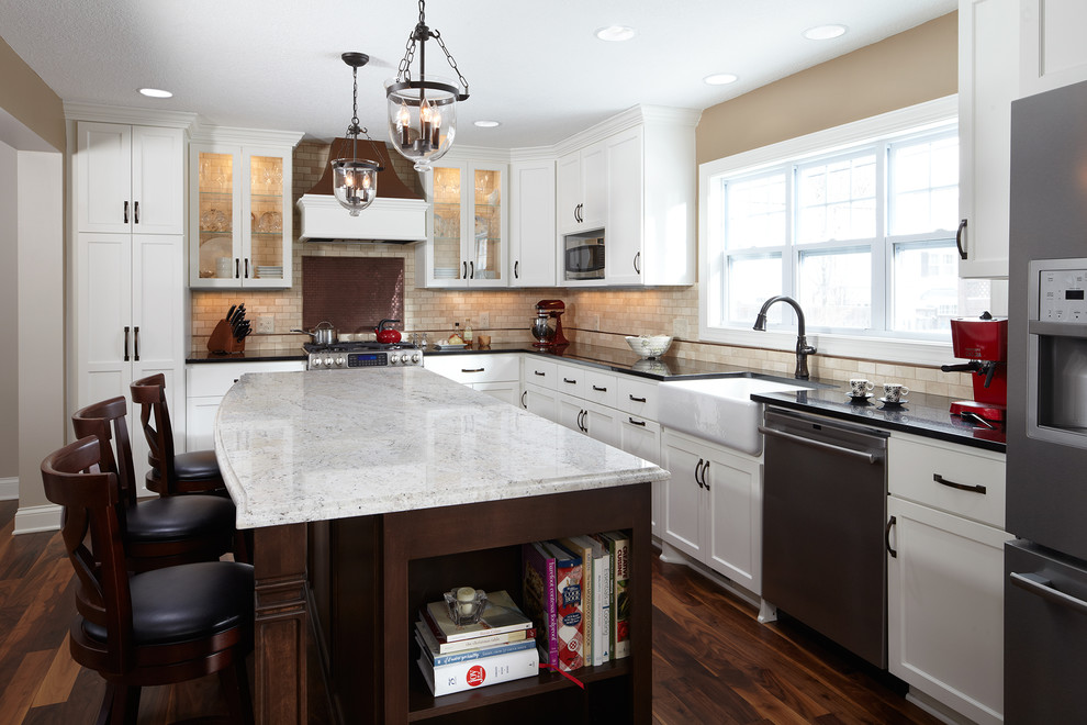 This is an example of a traditional kitchen in Minneapolis with a belfast sink, shaker cabinets, white cabinets, granite worktops, beige splashback, stainless steel appliances, medium hardwood flooring and an island.